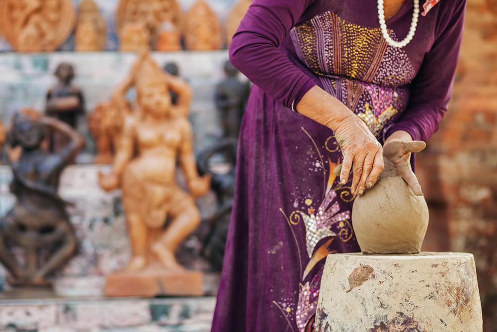 A woman in a purple outfit shaping a clay pot, with sculptures behind her